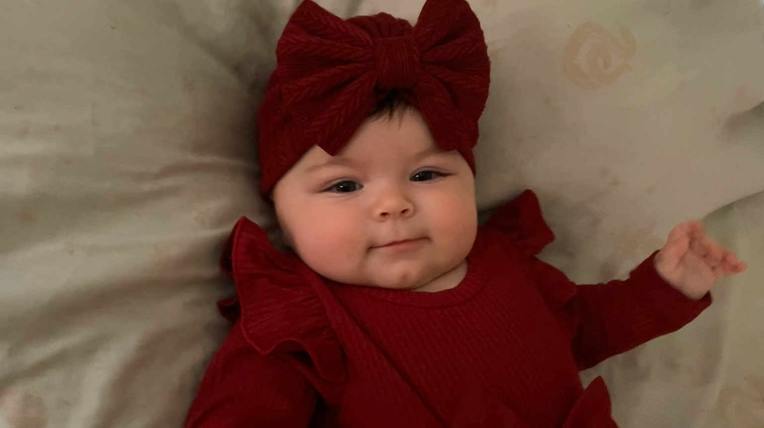 Ariane participe au concours pour gagner de l'argent avec cette photo : baby, infant, red_clothing, headband, bow, face, smile, lying_down, soft_surface, cute, child, portrait, indoors, young_child, warm_colors, adorable, chubby_cheeks, headwear, human, happy