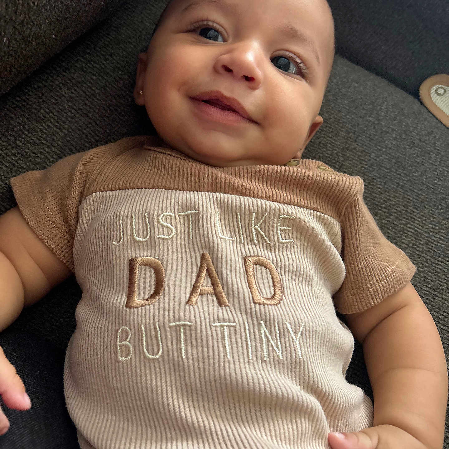 Adonai is registered to the contest to win money with this photo: arm, baby, casual, child, closeup, clothing, couch, cute, fabric, face, hand, happy, indoors, infant, person, portrait, ribbed_texture, smile, text_on_clothing, young_child