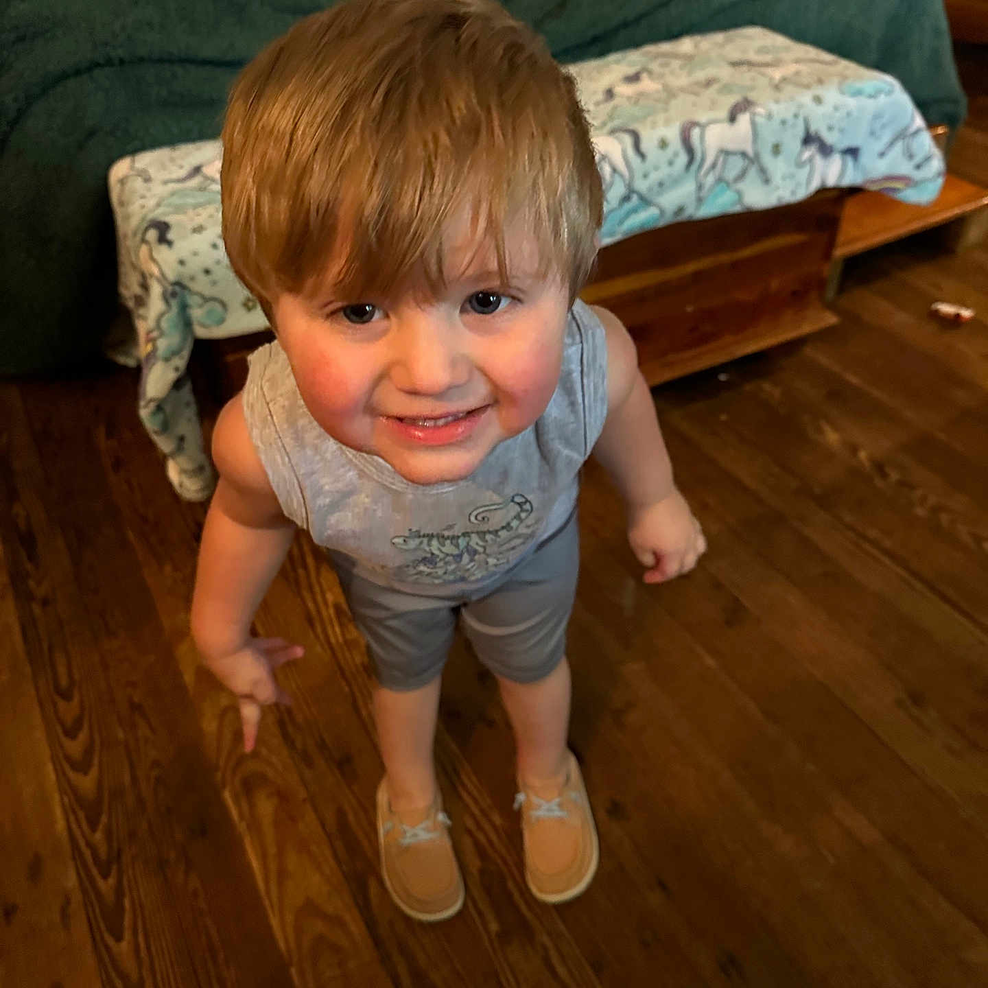 Karson is registered to the contest to win money with this photo: bed, blanket, blonde_hair, casual_clothing, child, cute, floor, furniture, happy, home, indoor, looking_up, person, portrait, shoes, shorts, smiling, tank_top, wooden_floor, young
