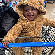 Kamari joined the competition — help win amazing prizes! baby, child, shopping_cart, grocery_store, fuzzy_clothing, hooded_jacket, brown_clothing, smiling, happy, cute, person, infant, indoor, retail, retail_environment, hand, face, apparel, seat, holding