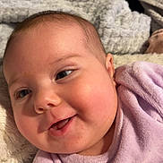 Elyana participe au concours pour gagner de l'argent avec cette photo : baby, blanket, cheeks, closeup, cozy, cute, expression, face, happy, head, indoors, infant, love_text, person, purple_clothing, skin, smiling, soft_texture, toddler, warm
