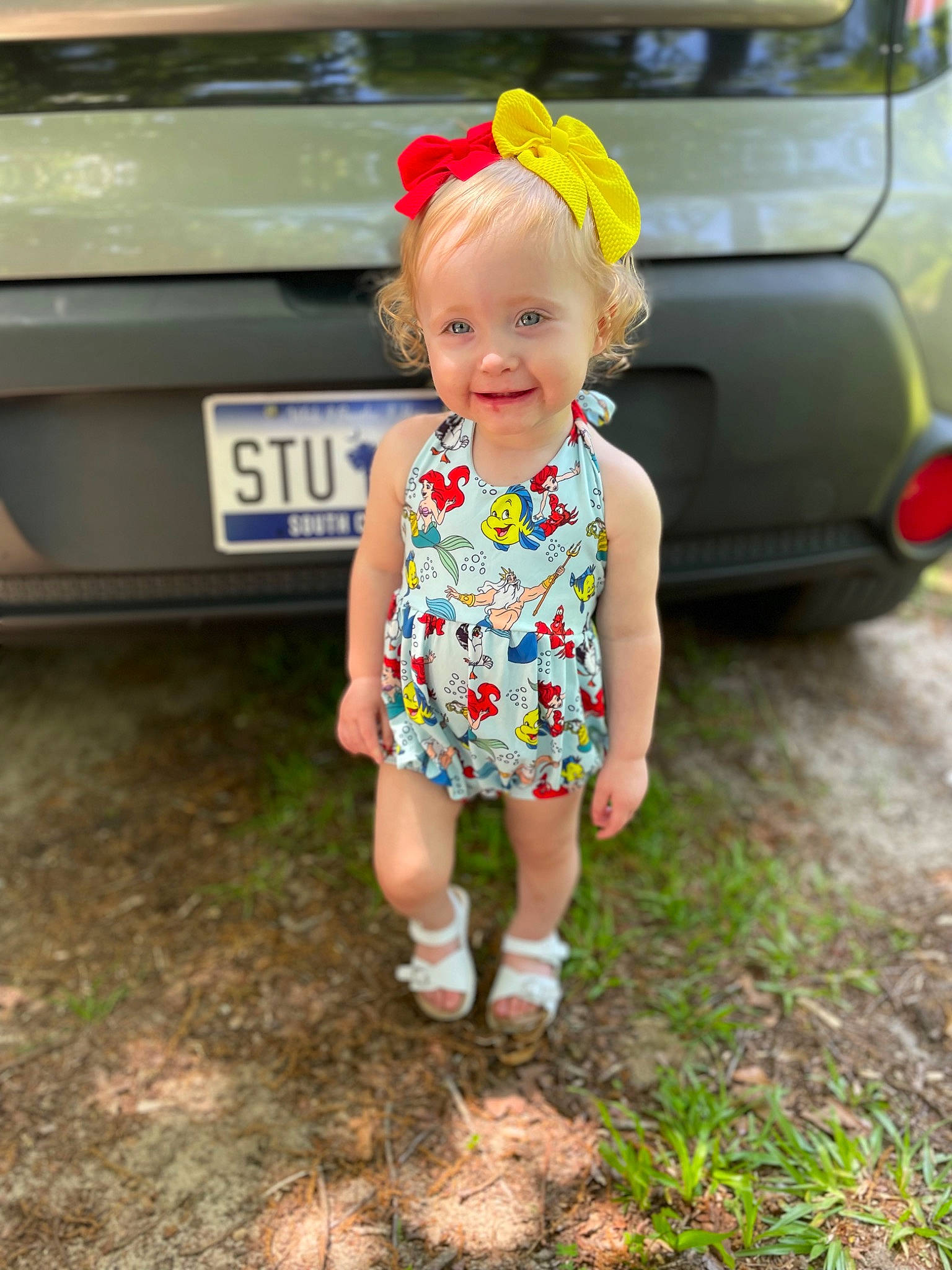 Madilynn is registered to the contest to win money with this photo: automotive_design, automotive_exterior, automotive_lighting, automotive_tail_brake_light, automotive_tire, baby_toddler_clothing, car, face, grass, hand, happy, hat, head, joy, motor_vehicle, person, pink, plant, smile, trunk