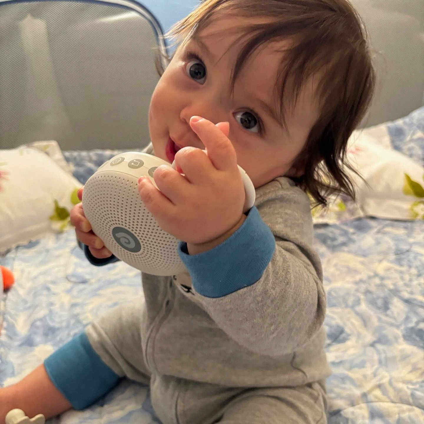Jack is registered to the contest to win money with this photo: baby, child, infant, toy, speaker, bed, bedding, blue, grey, clothing, face, hand, cute, indoors, playing, sitting, person, young, expression, home