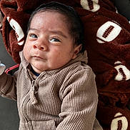 Thiago is registered to the contest to win money with this photo: baby, infant, child, portrait, face, eyes, hair, sweater, knitwear, zipper, blanket, football_pattern, brown, cozy, indoor, sitting, close_up, looking_at_camera, adorable, photography