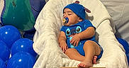 Thiago joined the competition — help win amazing prizes! baby, sleeping, infant, stitch, disney, blue_outfit, blue_hat, pacifier, white_chair, blanket, balloons, blue_balloons, stuffed_toy, plush_toy, birthday_setup, milestone_photo, letter_board, indoor, portrait, decorations