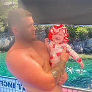 Dolly-Gee is registered to the contest to win money with this photo: man, baby, tattoo, swimsuit, hat, boat, water, swimming, rocks, trees, outdoor, sunlight, holding, child, smile, nature, summer, vacation, people, happy