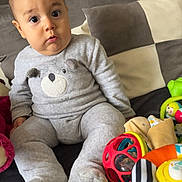 Zayan participe au concours pour gagner de l'argent avec cette photo : baby, bear_design, blanket, child, colorful_toys, couch, cute, expression, furniture, gray_outfit, home, indoor, infant, person, pillow, plush, sitting, soft_lighting, toys, wide_eyes