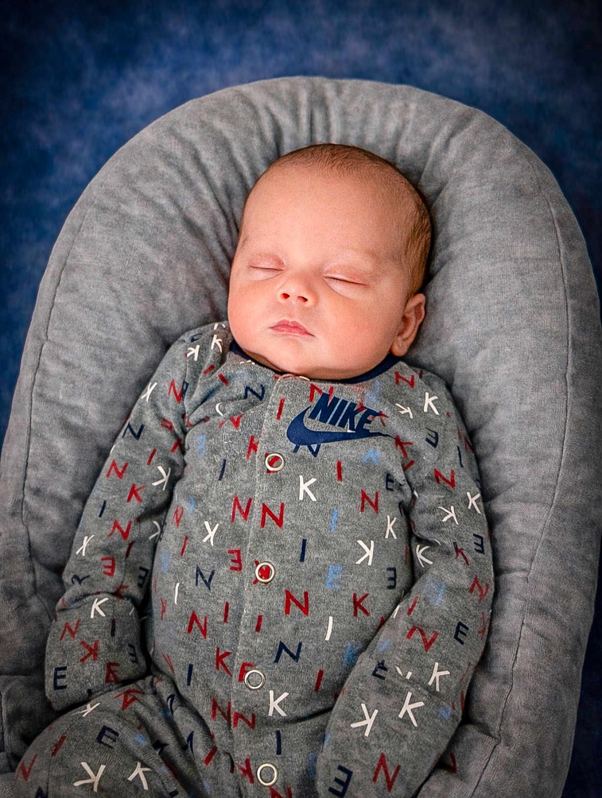 Camden is registered to the contest to win money with this photo: baby, sleeping, onesie, nike, gray, cushion, infant, soft, comfortable, cozy, child, portrait, peaceful, cute, clothing, indoor, relaxing, newborn, rest, face