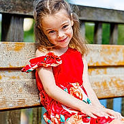 Kaytana participe au concours pour gagner de l'argent avec cette photo : child, girl, smile, red_dress, flowers, bench, wood, outdoor, sunlight, happy, portrait, nature, grass, summer, casual_clothing, sitting, young, cute, daylight, background_blur
