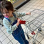 casual_clothing, child, curious, denim, floor_tiles, footwear, grocery_store, indoor, long_sleeve_shirt, overalls, pacifier, person, produce, refrigerator_case, shopping, shopping_cart, supermarket, toddler, toy_cart, young_child
