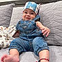 baby, denim_overalls, headscarf, smiling, couch, blanket, bracelet, foot, hand, quilted, indoor, child, cute, apparel, portrait, infant, comfortable, happy, clothing, relaxed