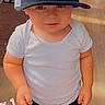 athletic_clothing, baseball_cap, bengals, child, eyes, face, football, furniture, hands, heart_sticker, home, indoors, portrait, shorts, smiling, sports_fan, standing, toddler, white_shirt, wood_floor
