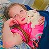 animal, bed, blanket, casual, cat, child, comfort, cozy, cute, floral_pattern, hand, home, indoor, pink_shirt, portrait, relaxed, resting, snuggling, soft_lighting, young_girl