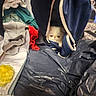Binx is registered to the contest to win money with this photo: bag, cat, closeup, clothing, curious, fabric, folded_clothes, green_cloth, grey_cloth, hand, hidden, indoor, peek, plastic_sheet, pocket, red_cloth, texture, white_cat, yellow_object, zipper