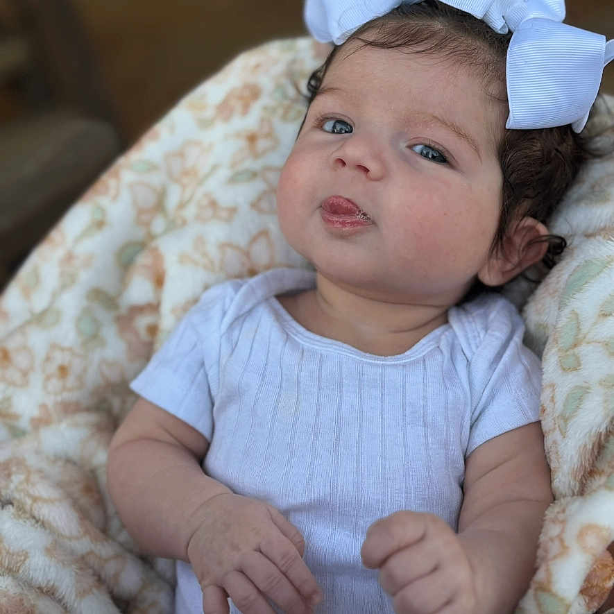 Leigha is registered to the contest to win money with this photo: baby, bodypart, bonnet, cap, clothing, couch, face, finger, furniture, hand, happy, hat, head, newborn, person, photography, portrait, sitting, smile, t_shirt