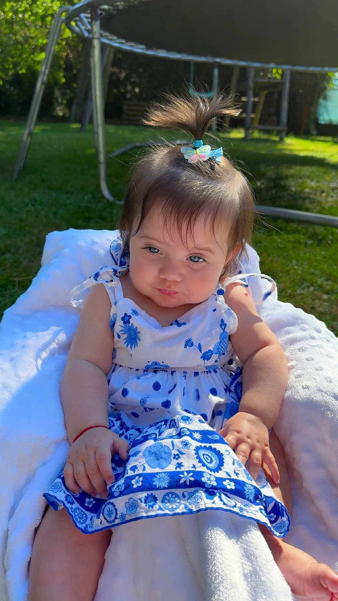 Sofia a rejoint le concours — aidez-le/la à gagner de superbes lots ! baby, child, girl, outdoor, sunlight, dress, blue_and_white, floral_pattern, blanket, grass, hair_clip, pony_tail, cute, sitting, person, nature, garden, happy, summer, infant