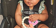 Olivia is registered to the contest to win money with this photo: baby, child, car_seat, teething_toy, headband, bow, infant, cute, curly_hair, sitting, straps, safety_harness, foot, hand, clothing, indoor, portrait, looking_up, skin, adorable