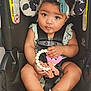 baby, child, car_seat, teething_toy, headband, bow, infant, cute, curly_hair, sitting, straps, safety_harness, foot, hand, clothing, indoor, portrait, looking_up, skin, adorable