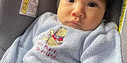 Kylo is registered to the contest to win money with this photo: baby, child, car_seat, sweater, winnie_the_pooh, warning_label, jeans, face, person, indoors, seat, clothing, cute, portrait, expression, young_child, infant, hair, sitting, serious