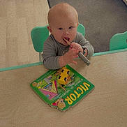 Aliciano participe au concours pour gagner de l'argent avec cette photo : baby, child, table, book, toy_car, wooden_stick, shoes, floor, mat, chair, indoor, play, curious, young_child, person, reading_material, footwear, furniture, home, learning