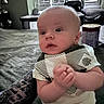 Tyson is registered to the contest to win money with this photo: baby, child, infant, portrait, sitting, hands_clasped, curious, calm, indoors, bedroom, furniture, bed, blanket, window, shutters, clothing, striped_shirt, short_sleeves, face, photography