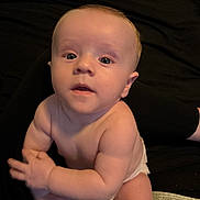 Tyson joined the competition — help win amazing prizes! baby, infant, child, portrait, sitting, diaper, face, eyes, curious, indoors, couch, dark_background, warm_lighting, close_up, photography, skin, hands, legs, carpet, baby_portrait