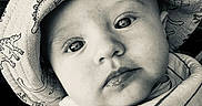 Tyson is registered to the contest to win money with this photo: baby, infant, child, portrait, face, eyes, wide_eyed, looking_at_camera, hat, dinosaur_pattern, blanket, striped_blanket, seated, close_up, black_and_white, indoor, cozy, soft_lighting, photography, calm