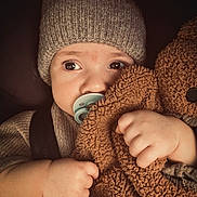Emilio a rejoint le concours — aidez-le/la à gagner de superbes lots ! baby, child, pacifier, hat, knit_hat, sweater, teddy_bear, plush_toy, close_up, cute, infant, hand, face, portrait, warm, soft_texture, cozy, indoor, expression, young