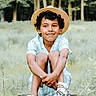 child, boy, smiling, hat, straw_hat, curly_hair, tree_stump, outdoor, nature, greenery, grass, casual_clothing, short_sleeves, shoes, white_shoes, patterned_shoes, happy, sitting, portrait, daylight
