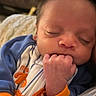 baby, sleeping, infant, close_up, hand, fist, face, blue_clothing, orange_clothing, cozy, newborn, peaceful, portrait, child, young, resting, indoors, soft_light, cute, person