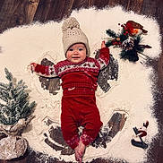 Amelie is registered to the contest to win money with this photo: baby, infant, floor, wooden_floor, powder, angel_shape, festive_clothing, red_pajamas, knit_hat, pine_tree, holiday_decor, toy_bird, toy_snowman, smiling, indoors, winter_theme, christmas, cute, child, playful