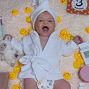 Riana is registered to the contest to win money with this photo: baby, smiling, white_robe, towel_turban, rubber_duck, makeup_brush, makeup, stuffed_toy, blanket, diaper, happy, infant, cosmetics, soft_texture, lying_down, cute, skincare, child, yellow, playful