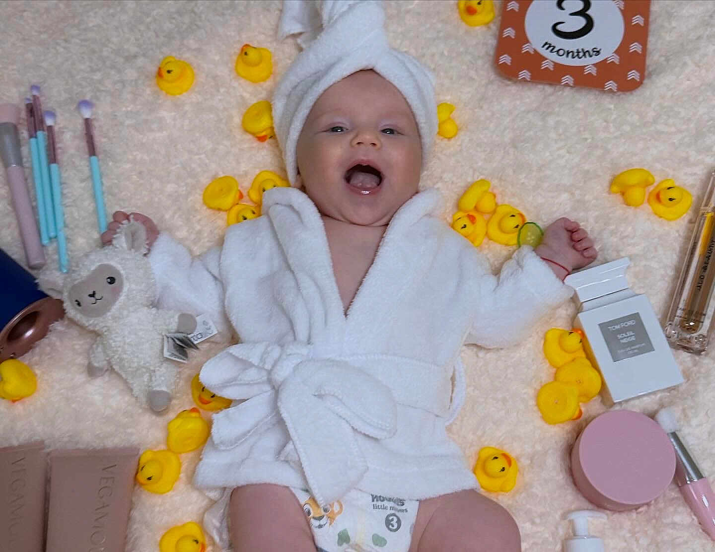 Riana is registered to the contest to win money with this photo: baby, smiling, white_robe, towel_turban, rubber_duck, makeup_brush, makeup, stuffed_toy, blanket, diaper, happy, infant, cosmetics, soft_texture, lying_down, cute, skincare, child, yellow, playful
