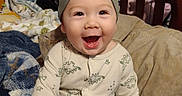 Thomas joined the competition — help win amazing prizes! baby, infant, smiling, dinosaur_print, onesie, beanie, bed, blanket, pillow, happy, child, indoors, cute, person, sleepwear, furniture, cozy, portrait, sitting, home