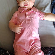 Thomas is registered to the contest to win money with this photo: baby, child, infant, pink_romper, smiling, lying_down, bed, clothing, person, cute, playful, indoor, skin, face, arm, legs, expression, happy, young, relaxed