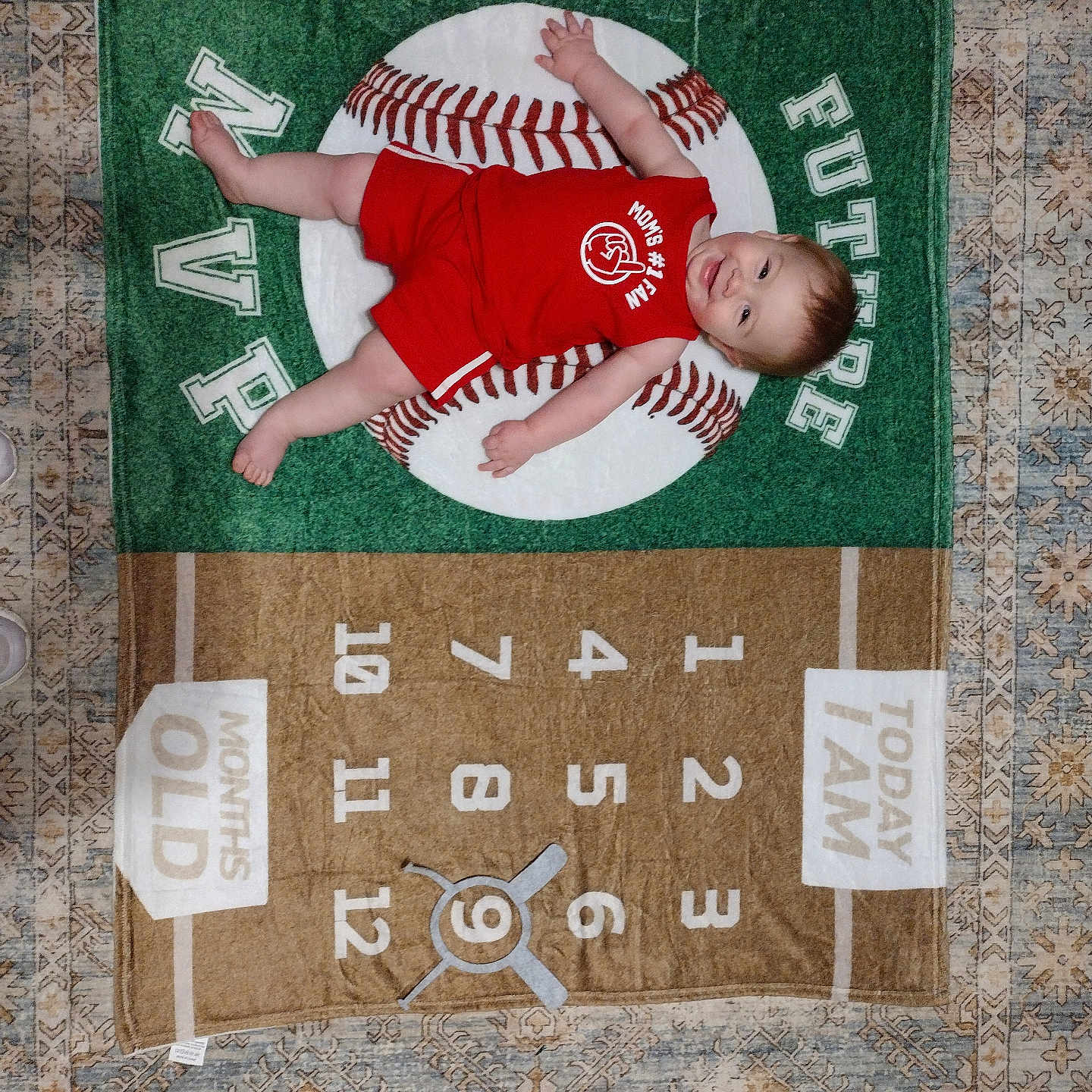 Thomas is registered to the contest to win money with this photo: baby, infant, red_clothing, milestone_blanket, baseball_theme, numbers, months_old, smiling, laying_down, carpet, floor, child, person, portrait, cute, indoors, happy, baby_boy, young_child, blanket
