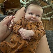 Milania joined the competition — help win amazing prizes! baby, smiling, infant, onesie, brown_clothing, leopard_print, heart_pattern, hand, lap, fingernails, backpack, floor, wooden_floor, furniture, table, indoor, portrait, cute, person, happy