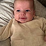 baby, infant, face, blue_eyes, smile, drool, beige_clothing, ribbed_fabric, cushion, soft_texture, closeup, portrait, child, cute, indoors, cozy, person, skin, head, newborn