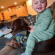 Junior is registered to the contest to win money with this photo: brown_dog, casual, child, couch, cozy, dog, family, furniture, green_pajamas, happy, home, indoor, living_room, pajamas, person, pet, pillows, smiling, toddler, young_child