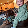 brown_dog, casual, child, couch, cozy, dog, family, furniture, green_pajamas, happy, home, indoor, living_room, pajamas, person, pet, pillows, smiling, toddler, young_child