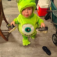 Junior is registered to the contest to win money with this photo: baby, blurred, carpet, child, clothing, costume, cute, floor, footwear, furniture, green, holding, home, indoor, monster, person, shoes, standing, toddler, toy