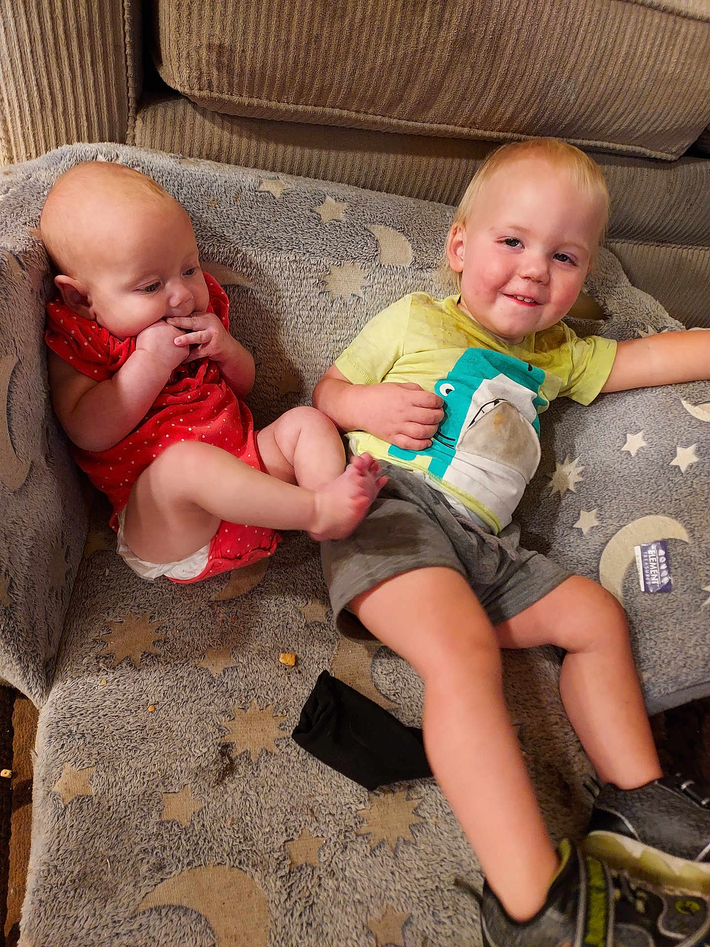 Junior is registered to the contest to win money with this photo: baby, toddler, child, couch, blanket, clothing, smile, face, footwear, sitting, indoor, fabric, pattern, toy, hand, leg, furniture, happy, casual, home