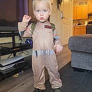 Junior is registered to the contest to win money with this photo: carpet, child, clothing, costume, couch, door, expression, floor, ghostbusters, hair, indoor, kitchen, living_room, person, shoes, standing, television, toddler, venkman, young_child