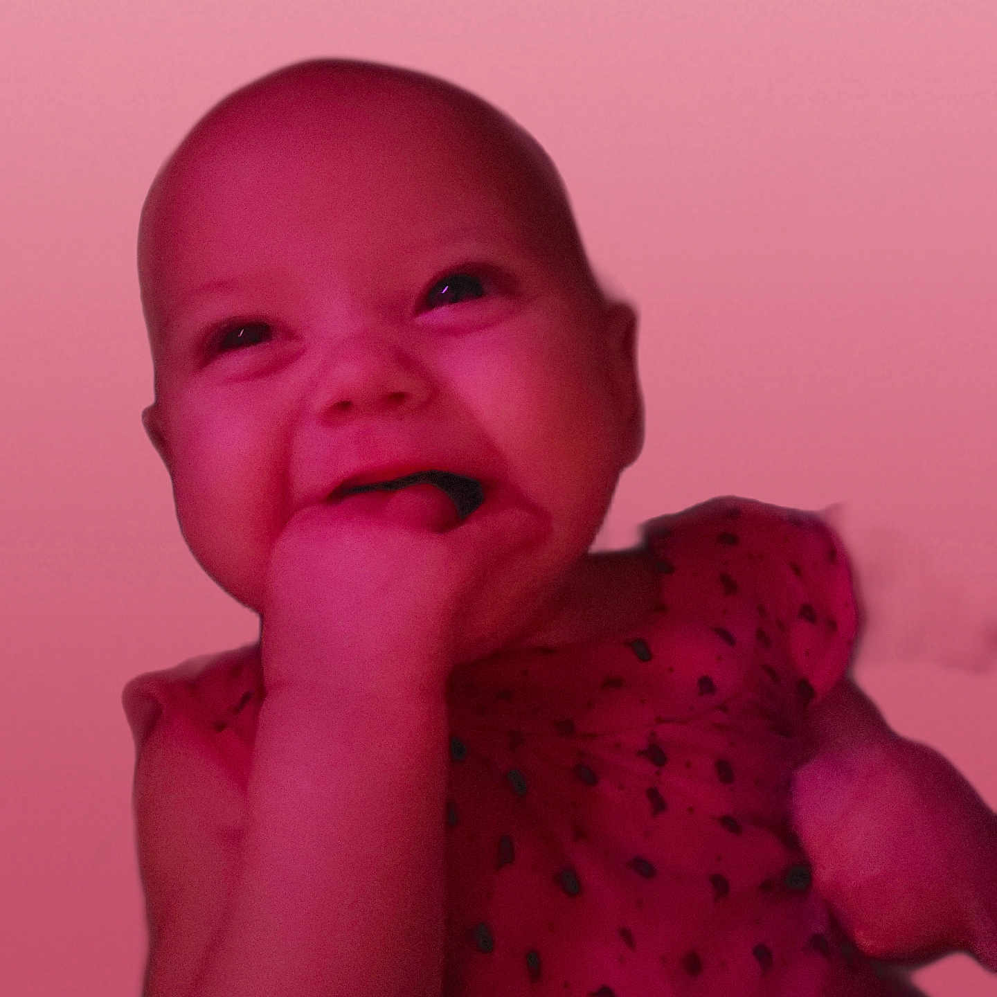 Maja is registered to the contest to win money with this photo: adorable, baby, cheeky, child, closeup, cute, expression, face, hand_in_mouth, happy, head, indoors, infant, pink_light, portrait, skin, sleeveless, smiling, wearing_dress, young_child