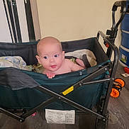 Maja Joy is registered to the contest to win money with this photo: baby, bald_head, blanket, curious, cute, eyes, fabric, face, floor, gaze, grip, hand, indoor, infant, metal_frame, portrait, storage_bins, towel, toy_wheel, wagon