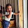 toddler, child, baby, standing, indoor, glass_door, hand, flooring, clothing, shorts, shirt, smile, face, hair, window, light, wood, person, safety_gate, barefoot