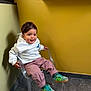 toddler, child, sitting, chair, transparent_chair, hoodie, pink_pants, green_sneakers, indoor, yellow_wall, floor, smiling, happy, casual_clothing, portrait, young_child, cute, playful, modern_interior, person