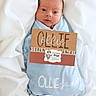 Ollie is registered to the contest to win money with this photo: newborn, baby, wrapped, blanket, blue_blanket, face, wide_eyes, infant, soft_fabric, name_card, pirate_theme, cute, portrait, lying_down, child, person, white_background, cardboard_sign, expression, small_baby