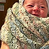newborn, baby, infant, smiling, face, portrait, knit_blanket, swaddled, hat, striped_hat, pastel, hospital, indoor, close_up, cozy, sleepy, eyes, nose, mouth, caregiver