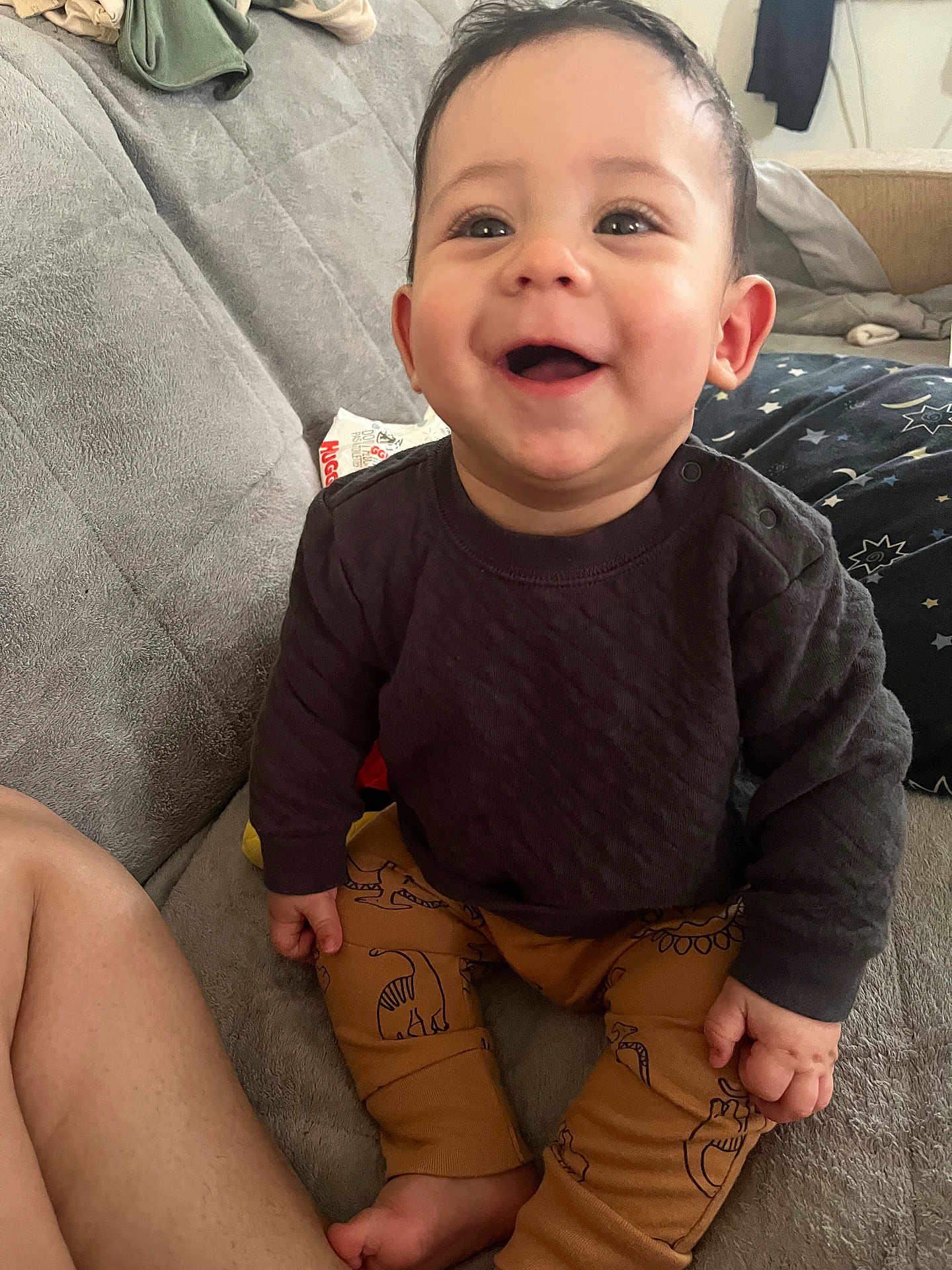 Kaine is registered to the contest to win money with this photo: baby, child, smiling, happy, sitting, indoor, clothing, pants, sweater, dinosaur_pattern, couch, furniture, skin, hand, foot, face, eyes, hair, cozy, comfort